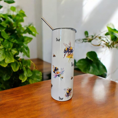 A tall, white tumbler decorated with colourful bee illustrations and a metal straw.