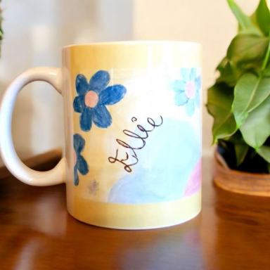 A personalised mug with blue flowers and the name "Ellie" on a colourful background.